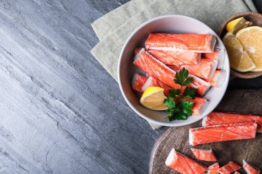 Gri arkaplanda yengeç çubukları ve limonlu düz kompozisyon, metin için boşluk