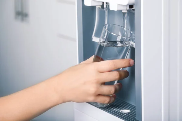 Woman filling glass with water cooler indoors, closeup. Refreshing drink