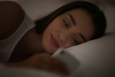 Geceleri yatakta akıllı telefon kullanan nomofobisi olan genç bir kadın. Uykusuzluk kavramı