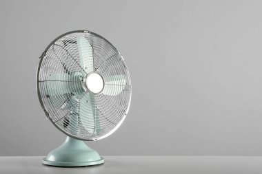 Açık gri arka plana karşı masada elektrikli vantilatör, mesaj için yer var. Yaz sıcağı