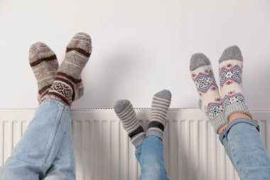 Beyaz duvarın yanındaki ısıtma kaloriferinde aile ısınma bacakları, yakın plan.