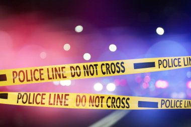 Sarı emniyet şeridi olay yerini izole ediyor. Şehir caddesinin bulanık görüntüsü, kırmızı ve mavi polis arabası ışıkları.