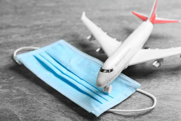 Toy airplane and medical mask on grey stone background, closeup. Travelling during coronavirus pandemic