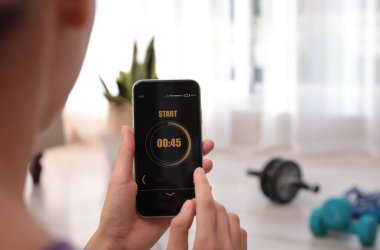 Genç bir kadın akıllı telefonunda spor uygulaması kullanıyor, kapalı mekanda, yakın plan. Metin için boşluk