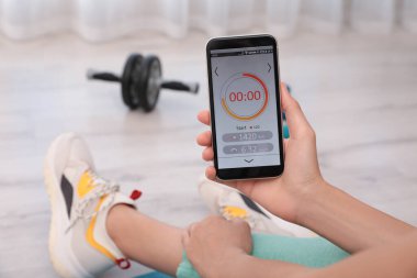 Genç bir kadın akıllı telefonunda spor uygulaması kullanıyor. Kapalı alanda.