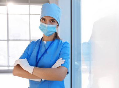 Tıbbi eldivenli, koruyucu maskeli ve kapalı alanda önlüklü bir doktor. Metin için boşluk