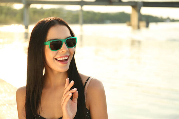 Красивая молодая женщина в стильных солнечных очках возле реки. Пространство для текста