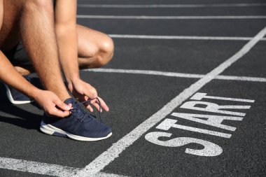Stadyumda başlama çizgisinin önünde ayakkabı bağlayan sporcu, yakın plan.