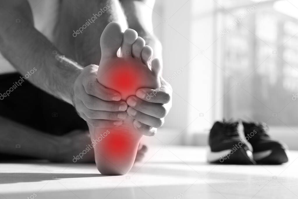 Man suffering from foot pain on floor indoors, closeup