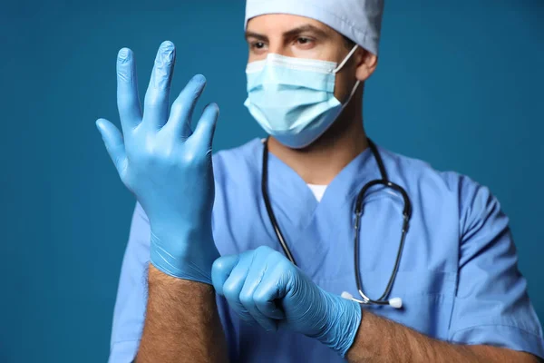 Dokter Beschermend Masker Zet Medische Handschoenen Tegen Blauwe Achtergrond — Stockfoto