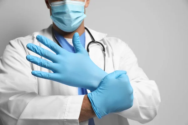 Dokter Beschermende Masker Zetten Medische Handschoenen Tegen Lichtgrijze Achtergrond Close — Stockfoto