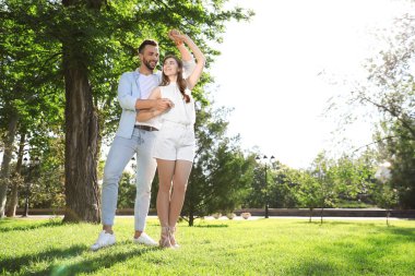 Güneşli bir günde parkta dans eden sevimli genç çift.