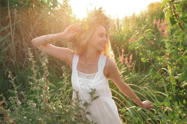 Güneşli bir günde, açık havada güzel çiçeklerden yapılmış çelenk giyen genç bir kadın.