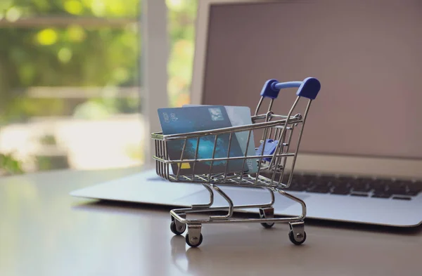 Internet shopping. Small cart with credit cards and laptop on table indoors