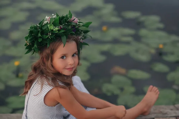 池の近くに美しい花で作られた花輪を着てかわいい女の子 — ストック写真