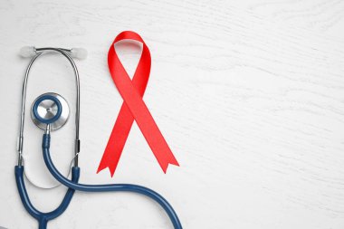 Beyaz ahşap arka planda kırmızı kurdele ve steteskop, yazı için yeri olan düz bir yer. AIDS Hastalığı Farkındalığı
