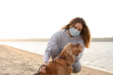 Sahilde İngiliz Cocker Spaniel 'i olan koruyucu maskeli kadın. COVID-19 salgını sırasında köpek gezdirme