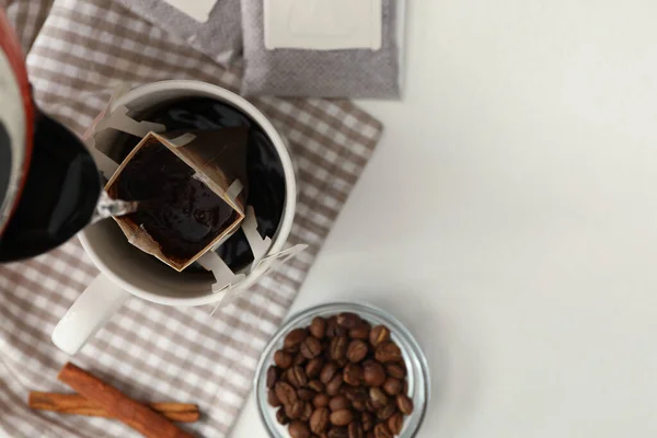 Pouring hot water into cup with drip coffee bag on white table, flat lay. Space for text