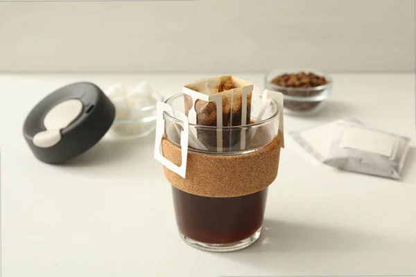 白いテーブルの上にドリップコーヒーバッグ付きガラスカップ — ストック写真