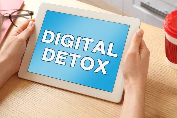 Woman using tablet computer with text Digital Detox at table, closeup
