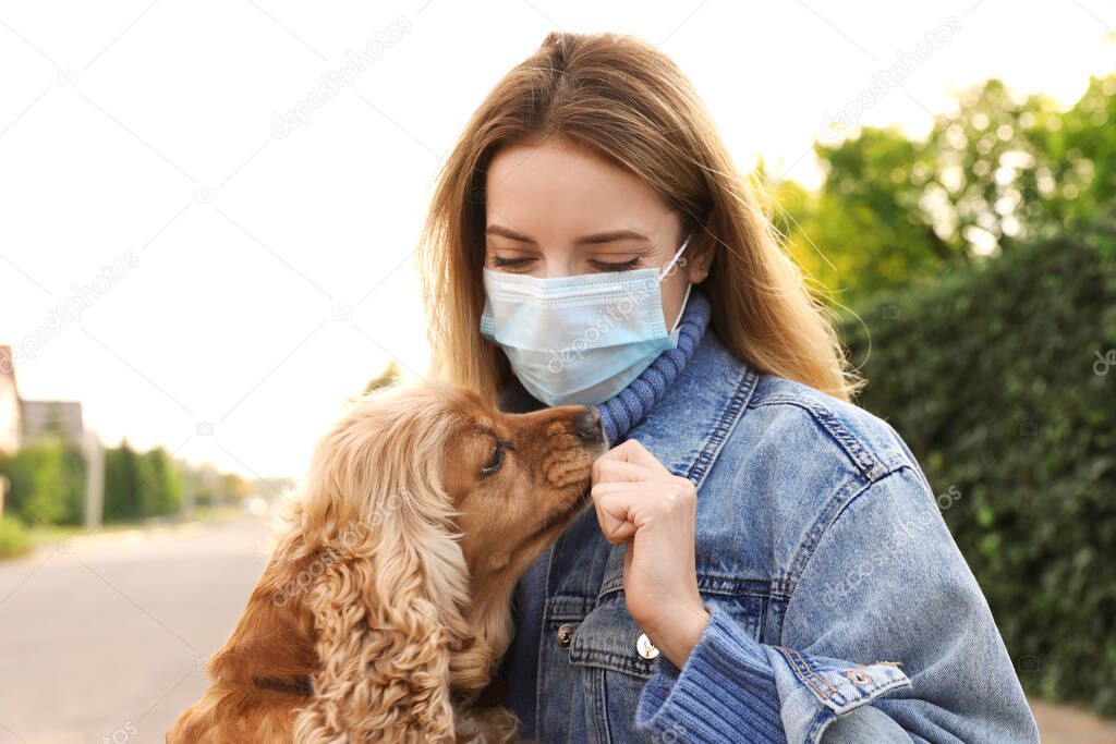 Woman in protective mask with English Cocker Spaniel outdoors. Walking dog during COVID-19 pandemic