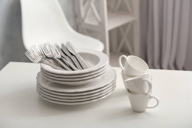 Set of clean dishware and cutlery on white table indoors clipart