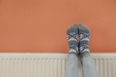 Renkli duvarın yanındaki ısıtma kaloriferinde bacakları ısıtan adam, yakın plan. Metin için boşluk