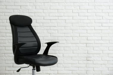 Beyaz tuğla duvarın yanında rahat bir ofis sandalyesi. Metin için boşluk