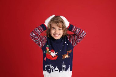 Kırmızı arka planda gülümseyen Noel süveteri içindeki şirin küçük kız.