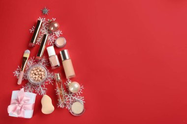 Kırmızı arka planda dekoratif kozmetik ürünlerinin Noel ağacı şekli, metin için yeri olan düz bir yer. Kış bakımı