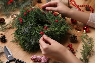 Çiçekçi, ahşap masada böğürtlenlerle güzel bir Noel çelengi yapıyor.