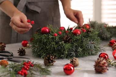 Çiçekçi, gri masada güzel bir Noel çelengi yapıyor.