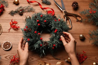 Çiçekçi güzel bir Noel çelengi yapıyor. Çam kozalakları ve böğürtlenlerle. Ahşap masada.