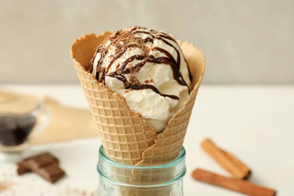 Delicious vanilla ice cream with toppings in wafer cone on white table, closeup