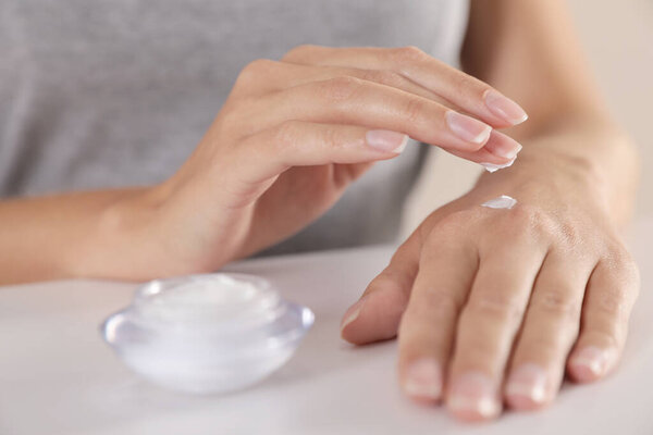 Young woman applying hand cream at table, closeup