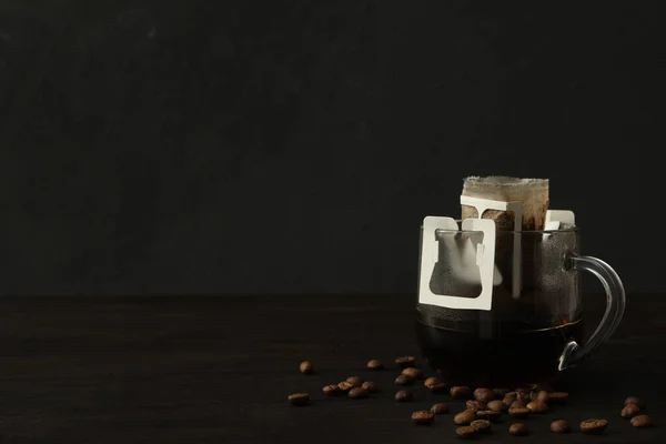 黒い木製のテーブルの上にドリップコーヒーバッグと豆とガラスカップ テキストのスペース — ストック写真