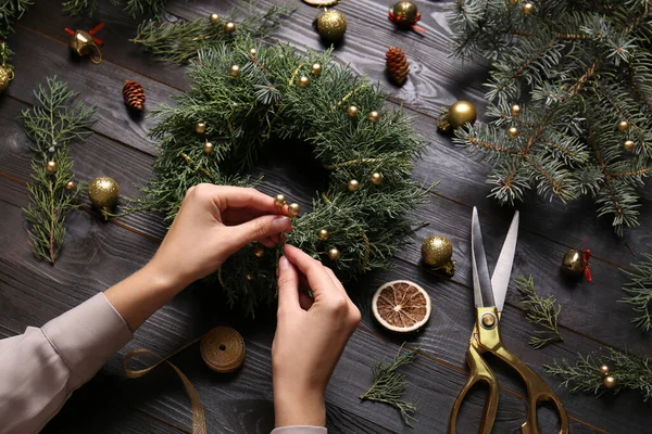 Florist making beautiful Christmas wreath at black wooden table, closeup