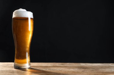 Koyu arka planda, ahşap masada soğuk, lezzetli bir bira. Metin için boşluk