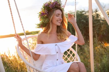 Dışarıda sallanan sandalyede çiçeklerden yapılmış çelenk giyen genç bir kadın.