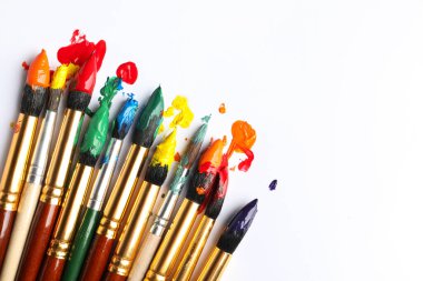 Beyaz arka planda renkli boyalı fırçalar, düz bir zemin. Metin için boşluk