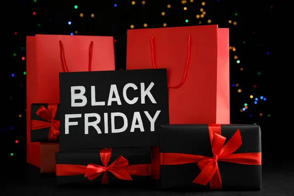 Paper shopping bags, gift boxes and phrase Black Friday against blurred lights