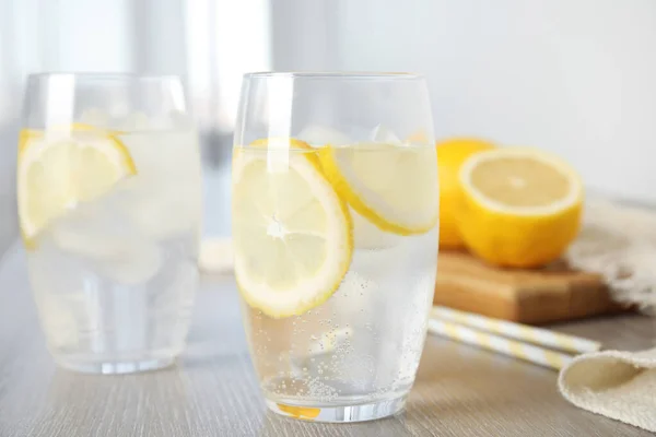 Soda water with lemon slices and ice cubes on wooden table indoors