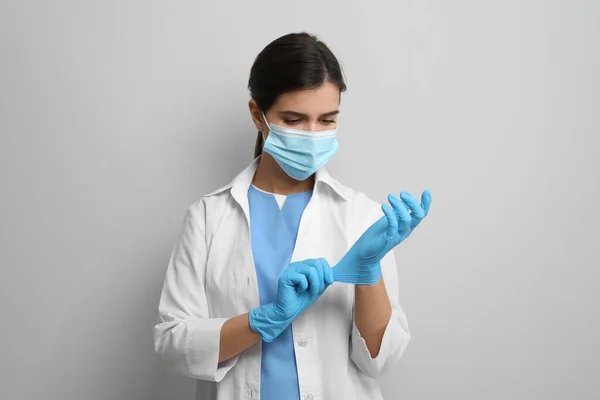 Doctor Beschermende Masker Zetten Medische Handschoenen Tegen Lichtgrijze Achtergrond — Stockfoto
