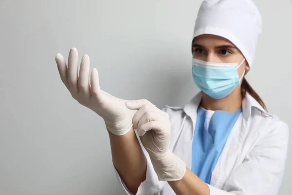 Doctor Beschermende Masker Zetten Medische Handschoenen Tegen Lichtgrijze Achtergrond — Stockfoto