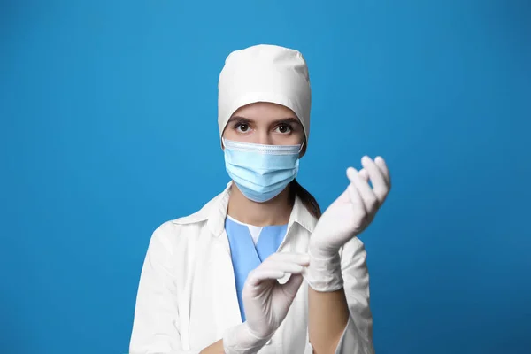 Dokter Beschermend Masker Zet Medische Handschoenen Tegen Blauwe Achtergrond — Stockfoto