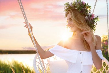 Dışarıda sallanan sandalyede çiçeklerden yapılmış çelenk giyen genç bir kadın.