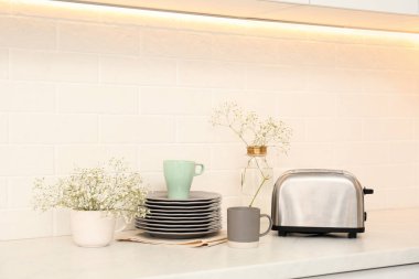 Modern ekmek kızartma makinesi, çanak çömlek ve çiçekler mutfakta tezgahta.