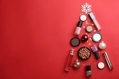 Kırmızı arka planda dekoratif kozmetik ürünlerinin Noel ağacı şekli, metin için yeri olan düz bir yer. Kış bakımı