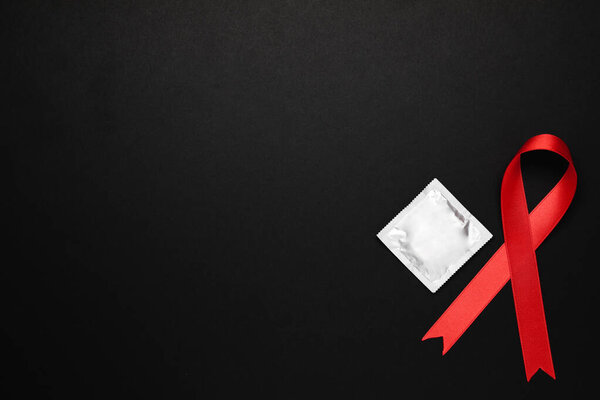Red ribbon and condom on black background, flat lay with space for text. AIDS disease awareness