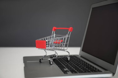 İnternet alışverişi. Masada gri arka planda küçük el arabası olan dizüstü bilgisayar